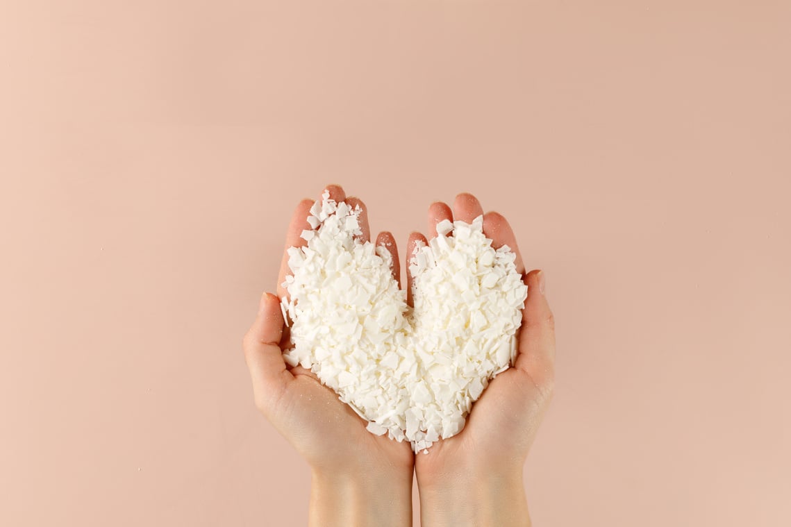 Hand with organic white Soy wax flakes for candles and sachet. Heart. Flatlay, top view. Natural soy and coconut wax for candlemaker.